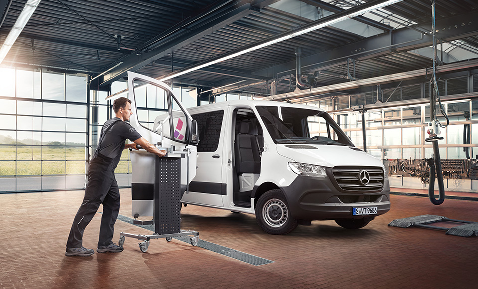 Werkstattmitarbeiter fährt einen Werkstattwagen zu einem weißen Sprinter